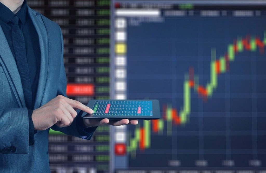 Homem de fato em pé a segurar num tablet. Elementos gráficos financeiros como pano de fundo.