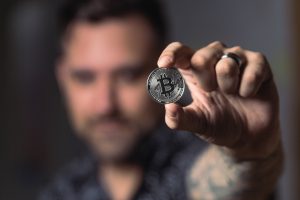 Homem a segurar numa moeda de Bitcoin prateada.