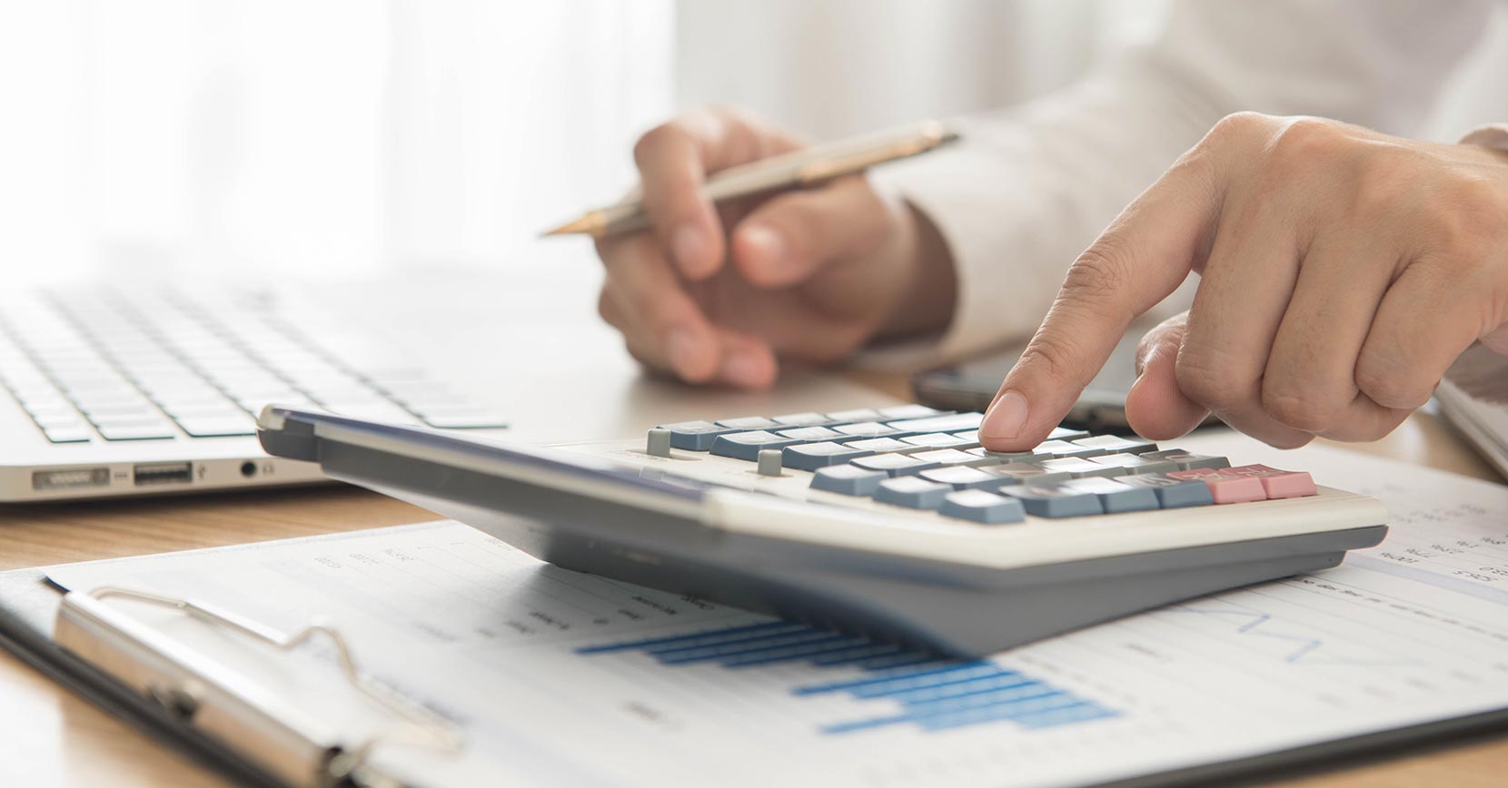 Homem a fazer contas numa calculadora que está em cima de uma mesa.