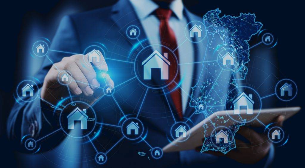 Homem de fato a apontar para um gráfico digital com transparência em primeiro plano com símbolos de casas e o mapa de portugal continental e ilhas.