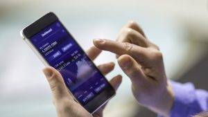 Mulher a segurar na mão um telemóvel com uma aplicação financeira aberta.