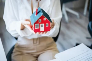 Mulher a segurar com as duas mãos uma casa miniatura