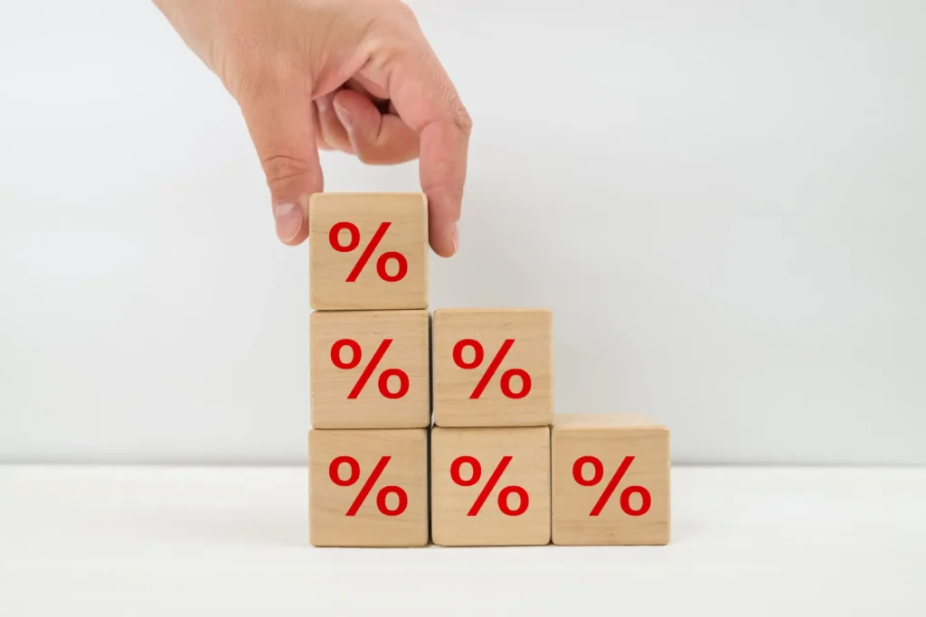 Mão de um homem a colocar cubos de madeira em "escadinha" com o símbolo de % desenhado em cada um